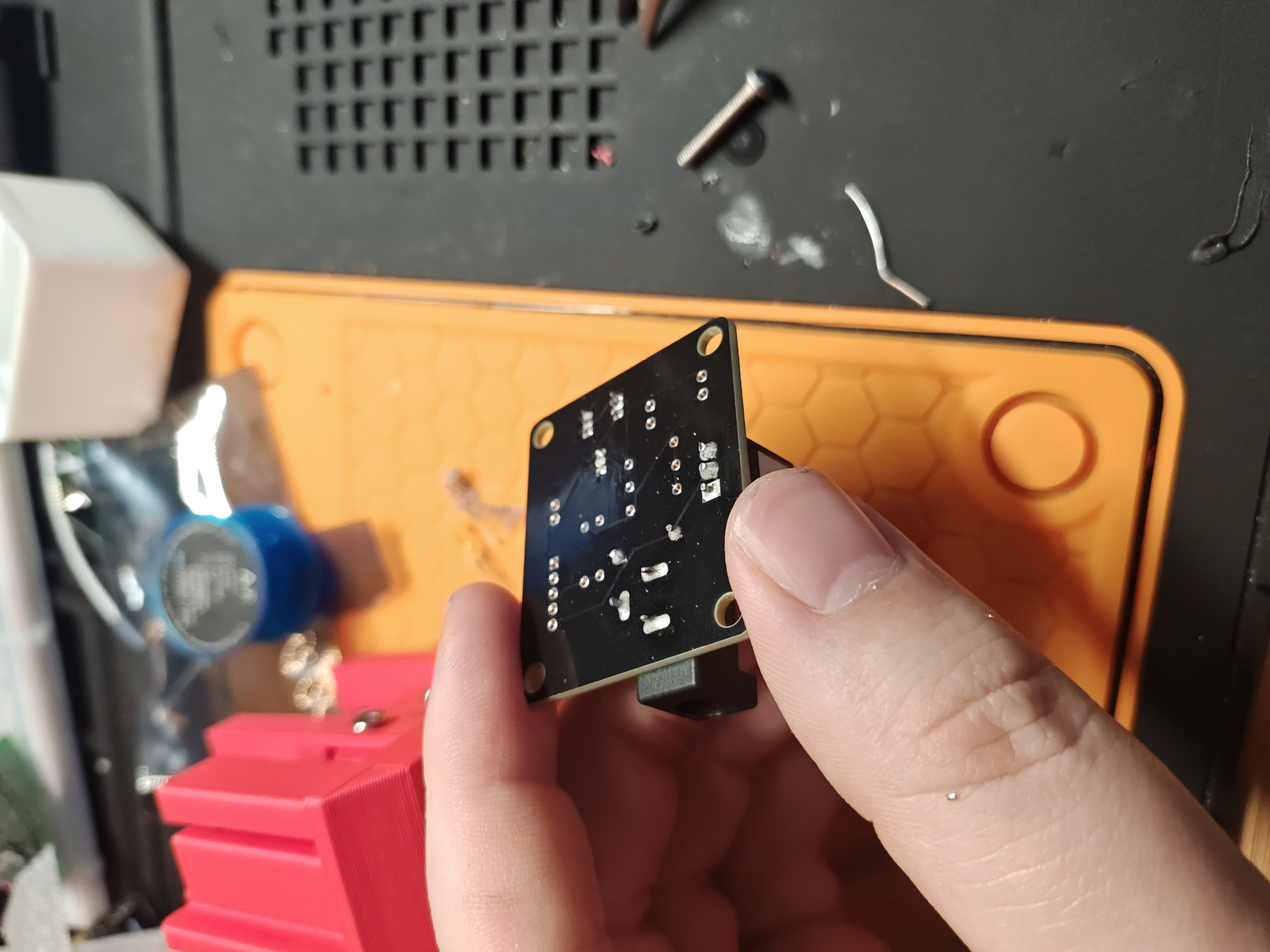 The back of the black board, showing rows of shiny soldered through-hole joints with trimmed leads, held between two fingers over a work mat.